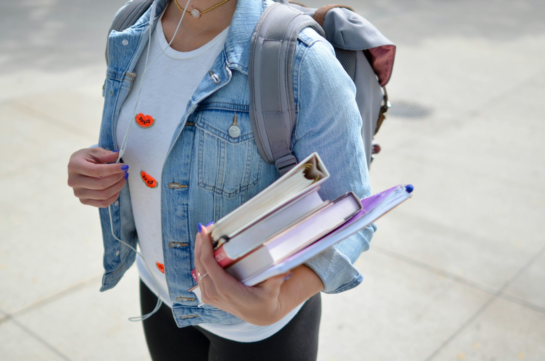 A student in a denim jacket carrying books and a backpack